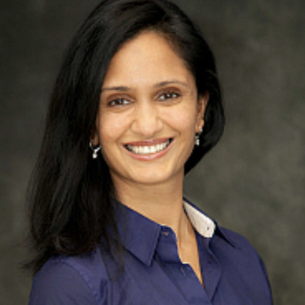 Headshot of Reena Abraham Bhatia smiling in front of a dark gray background